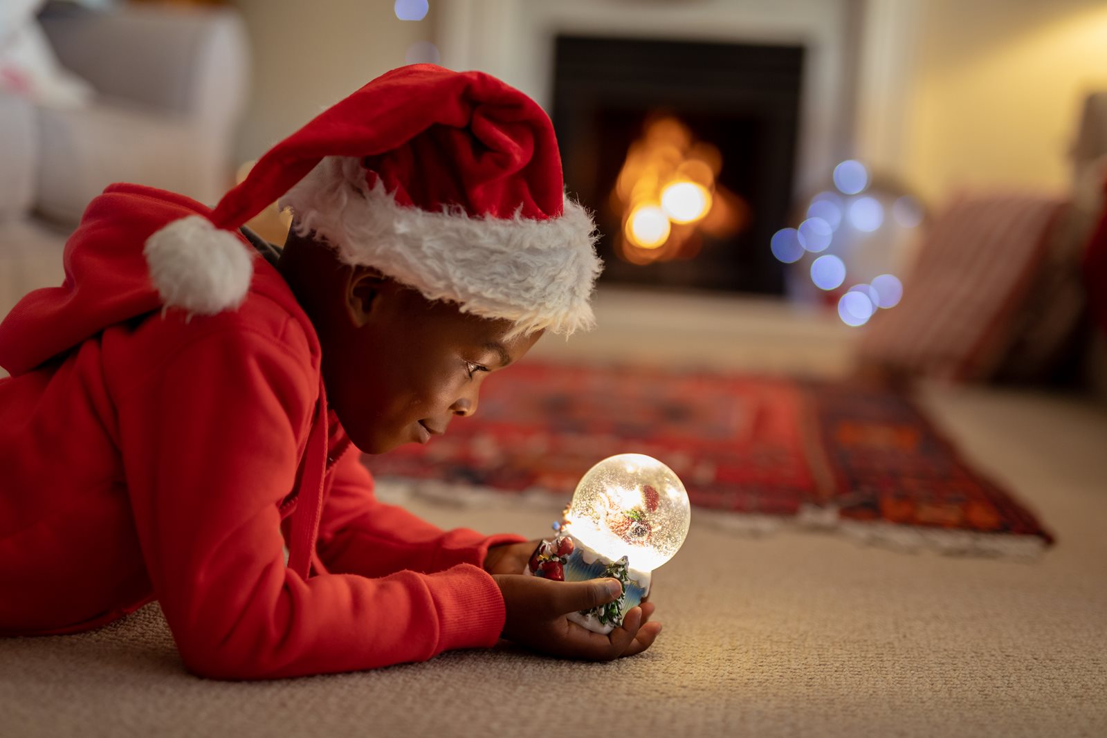 Child dressed in holiday attire looking in awe at a snow globe.