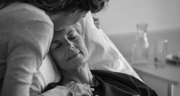 Woman comforting older woman in hospital bed